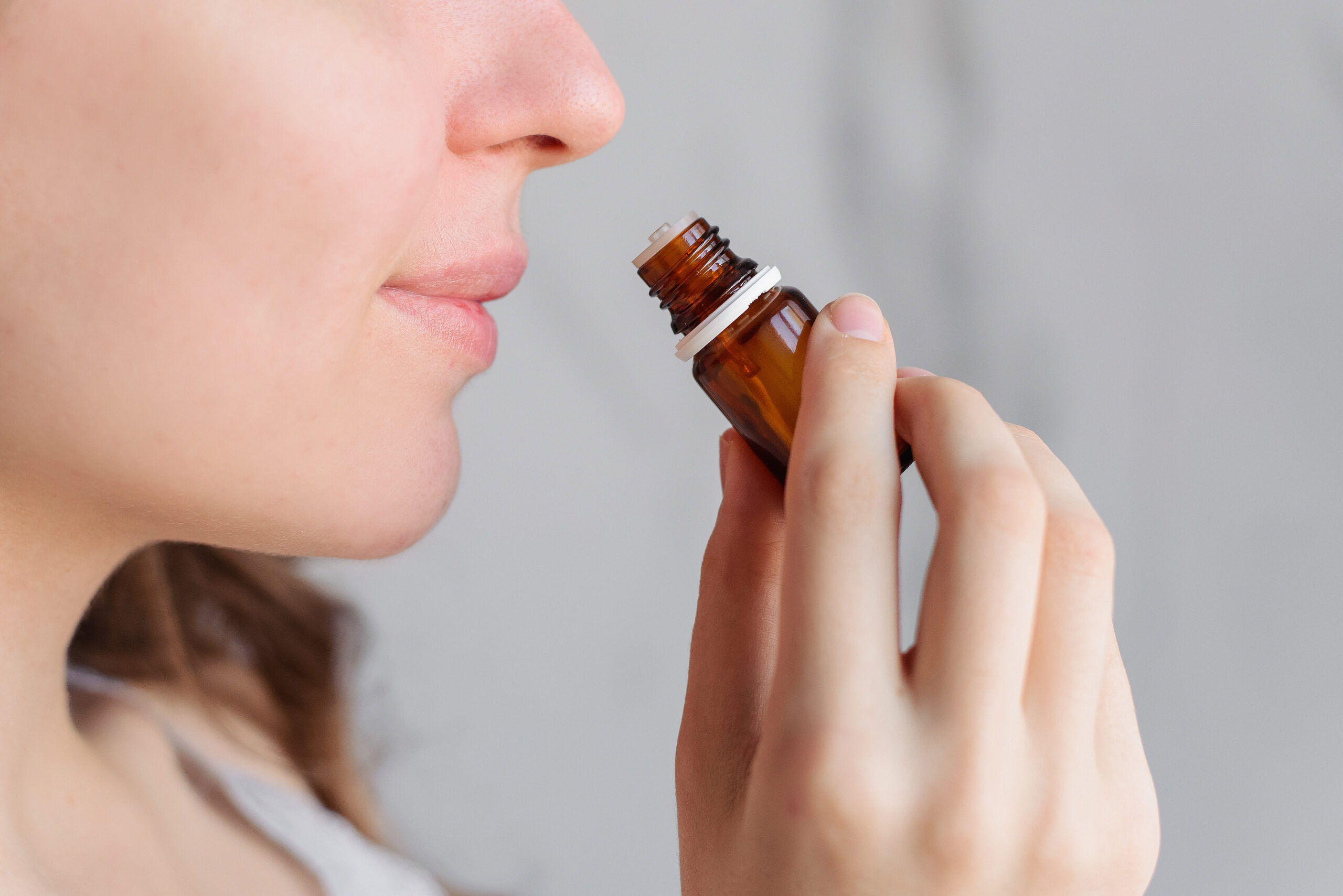 Aromatherapy: a girl with beautiful skin holds a bottle of essential oil near her nose and inhales. Close up, bright marble background. Full Moon Fire Ceremony